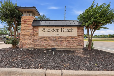 Sheldon Ranch sign on a brick wall with trees in the background.
