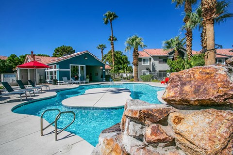 a swimming pool with a stone wall and chairs around it