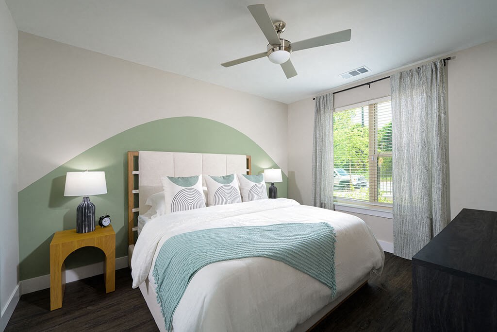 a bedroom with a green accent wall and a white bed with a tufted headboard at Verge Apartments in Atlanta, GA
