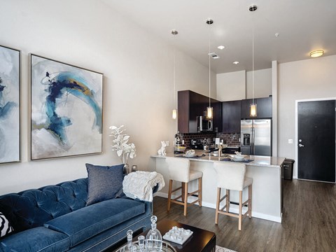 A modern living room with a blue couch and a dining area in the background.