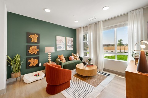 A living room with a green couch, a brown armchair, a wooden coffee table, and a large window with a view of the outdoors.