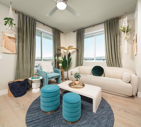 A living room with a white couch, blue ottoman, and a ceiling fan.