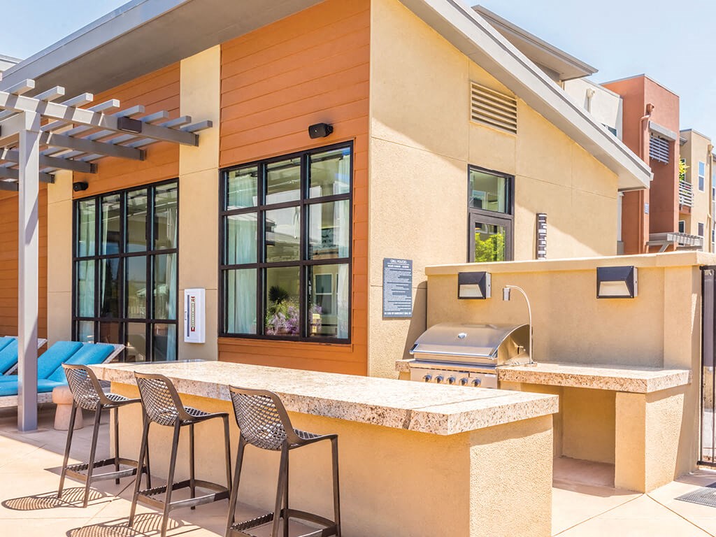 a patio with a bar and lounge chairs and a grill
