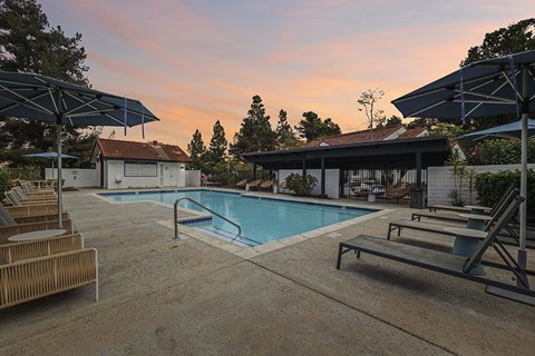 A pool area with sun loungers and a building in the background.