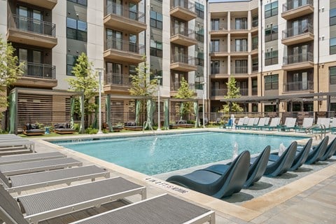A pool area with lounge chairs and apartment buildings in the background.