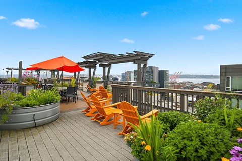 A wooden deck with orange chairs and a red umbrella overlooking a city skyline.
