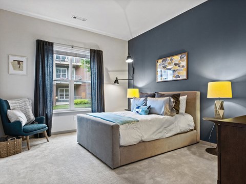 A bedroom with a large bed and a chair by the window.
