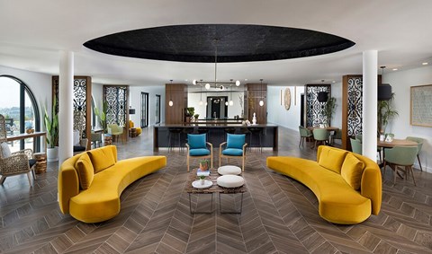 A modern living room with a large yellow sofa and a black circular ceiling light.