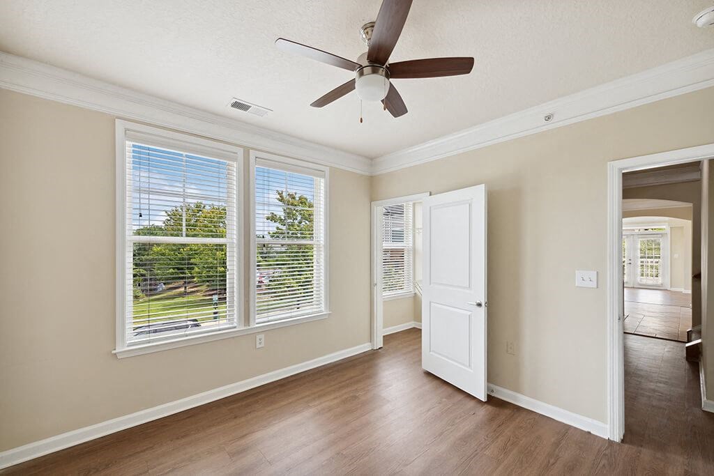 an empty living room with a ceiling fan and windows