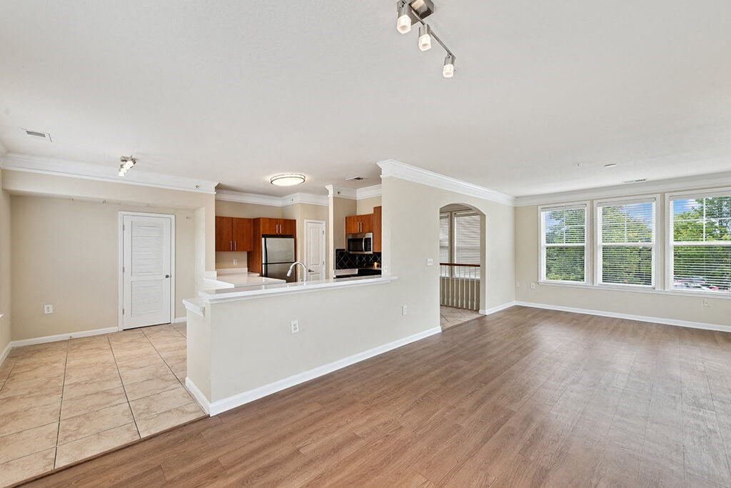 an empty living room with a kitchen and a large window