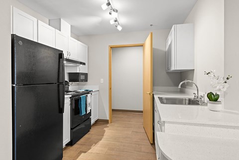 A black refrigerator is in a white kitchen with wooden floors.