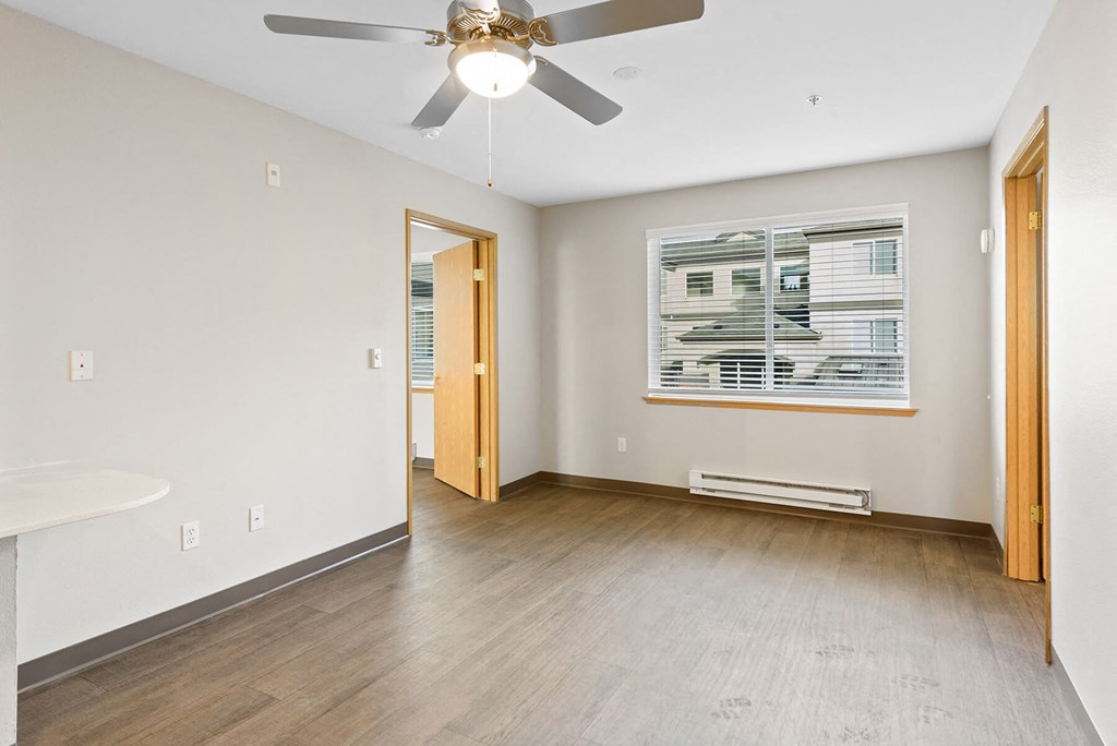 Retirement Homes In Federal Way - Spacious Living Room With New Wood-Style Plank Flooring, Ceiling Fan, Fresh Paint, And Window.