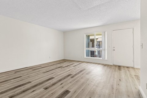 A room with wooden flooring and a window with a view of a hallway.