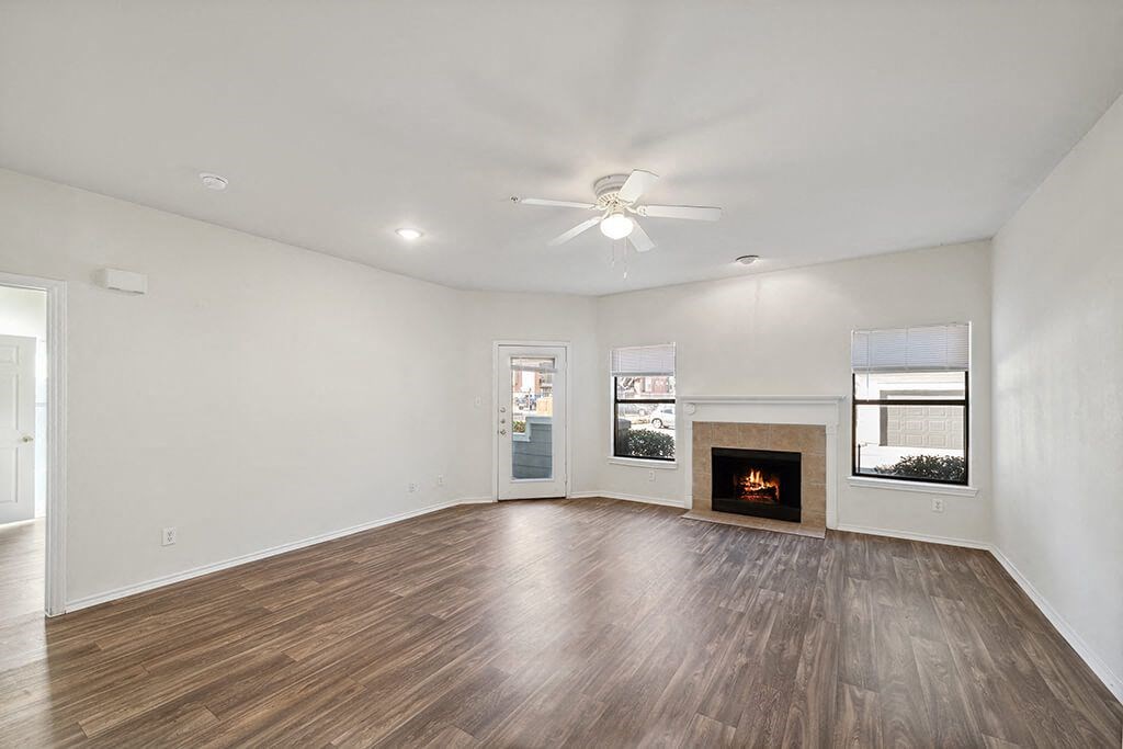 North Dallas Apartments for Rent - Tivoli - Open Concept Living Room with Tile Fireplace, Wood Plank Flooring, Large Windows, and Ceiling Fan