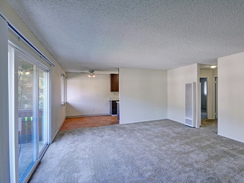 an empty living room with a sliding glass door to a kitchen