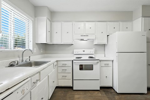 A white kitchen with a sink, stove, and refrigerator.