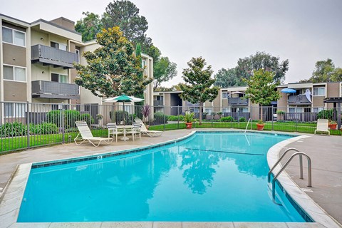 a swimming pool with chairs and umbrellas next to an apartment building