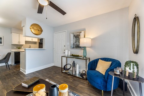a living room with a blue chair and a table and a kitchen