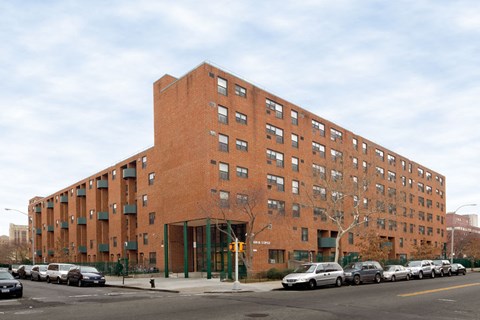A large red brick building with a green fence in front.