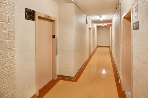 A long hallway with doors on either side and an exit sign at the end.