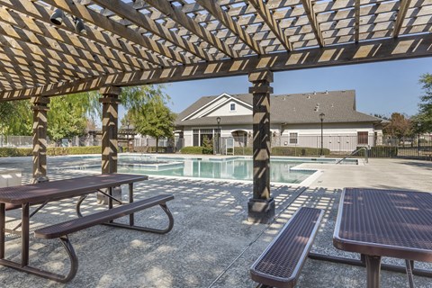 A wooden pergola over a picnic table with a pool in the background.