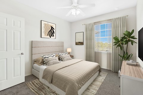 A bedroom with a large bed, a ceiling fan, and a window with curtains.