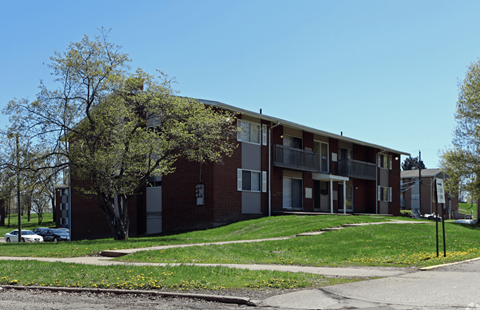 a red brick apartment building with a green lawn and a tree