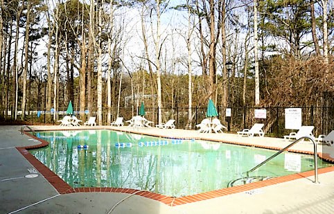 A pool surrounded by trees and chairs at Clarkston Station Apartments, Clarkston, Georgia