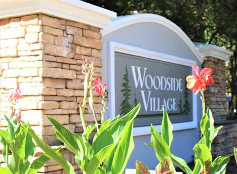 A sign that says Woodside Village with flowers in front at Woodside Village Apartments, Clarkston, 30021