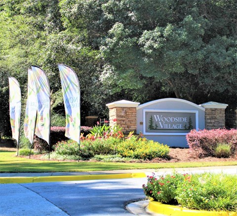 The entrance to Woodside Village is marked by a large sign and several flags at Woodside Village Apartments, Clarkston