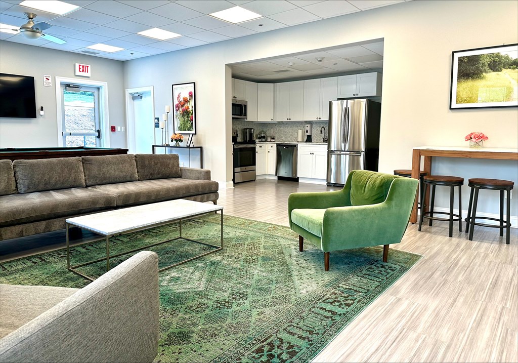 A community lounge with a comfortable sofa, chairs, a billiards table, a TV, a table with barstools, and access to a shared kitchen with full-size appliances and cabinets.