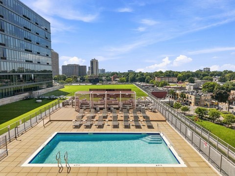 A rooftop pool with sun loungers and a view of the city.