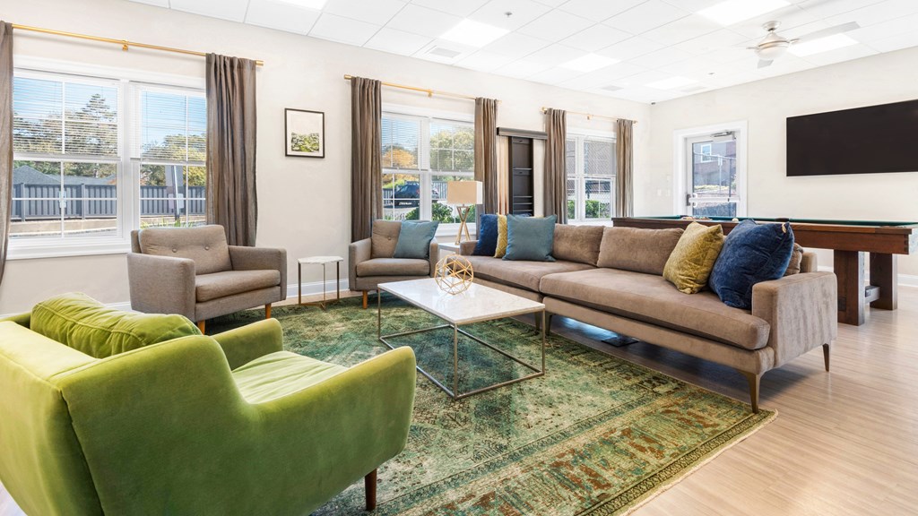 A community lounge with a comfortable sofa, chairs, a billiards table, a TV, and large windows.
