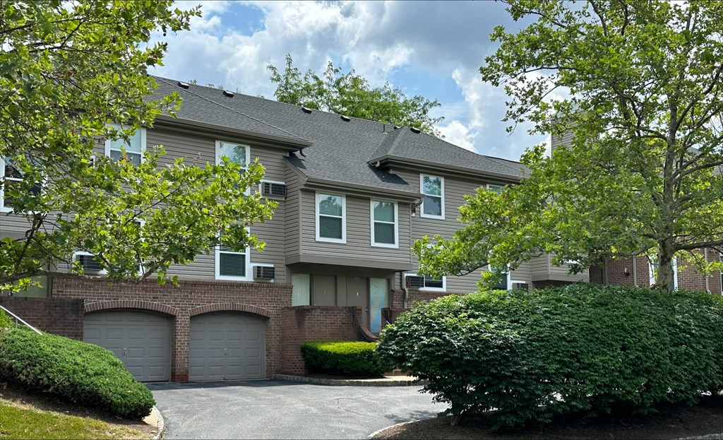 Exterior view of Everly Roseland's 3-story apartment buildings with garage parking surrounded by large trees, bushes, and grass.