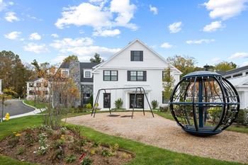 A white house with a black swing set in the front yard.