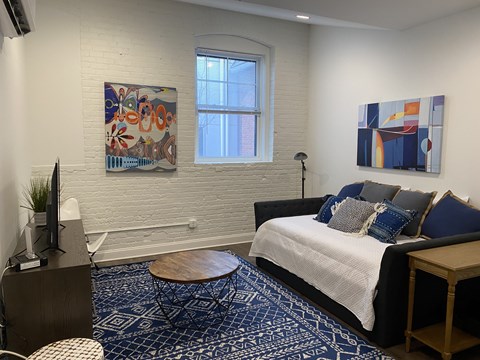 A bedroom with a bed, a chair, a table, a TV, and two paintings on the wall.