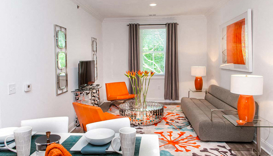 A living room with a grey couch, orange chairs, and a glass coffee table.