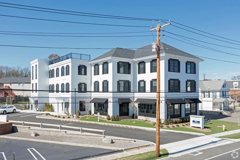 A white building with a grey roof and a sign in front of it.