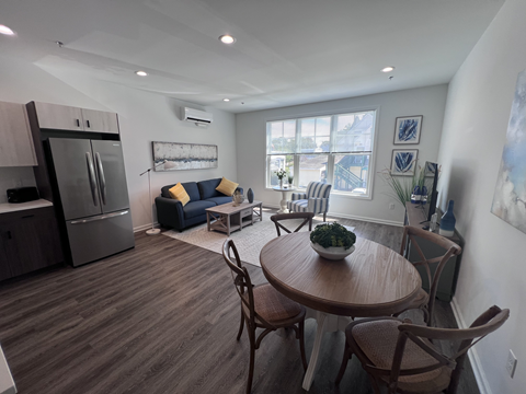 A kitchen with a refrigerator, a dining table with chairs, and a couch with pillows.