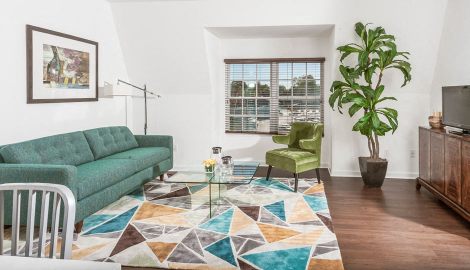 A living room with a green couch, a green chair, a glass coffee table and a potted plant.