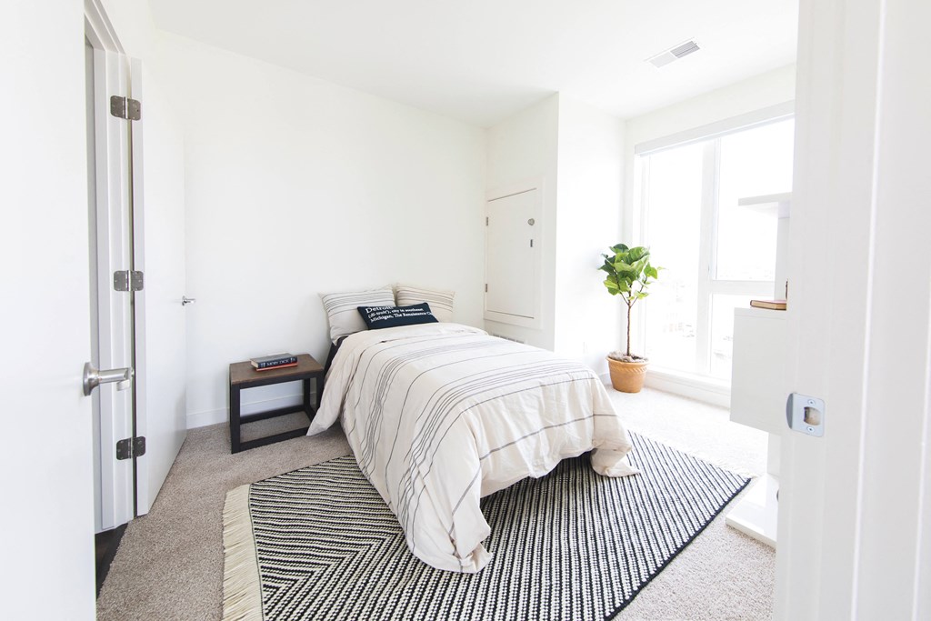 A bedroom with a bed, pillows, a small table, and a potted plant.