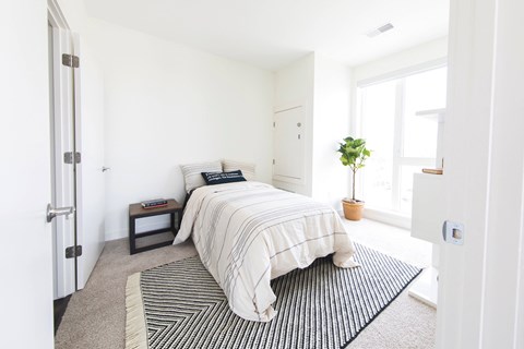 A bedroom with a bed, pillows, a small table, and a potted plant.