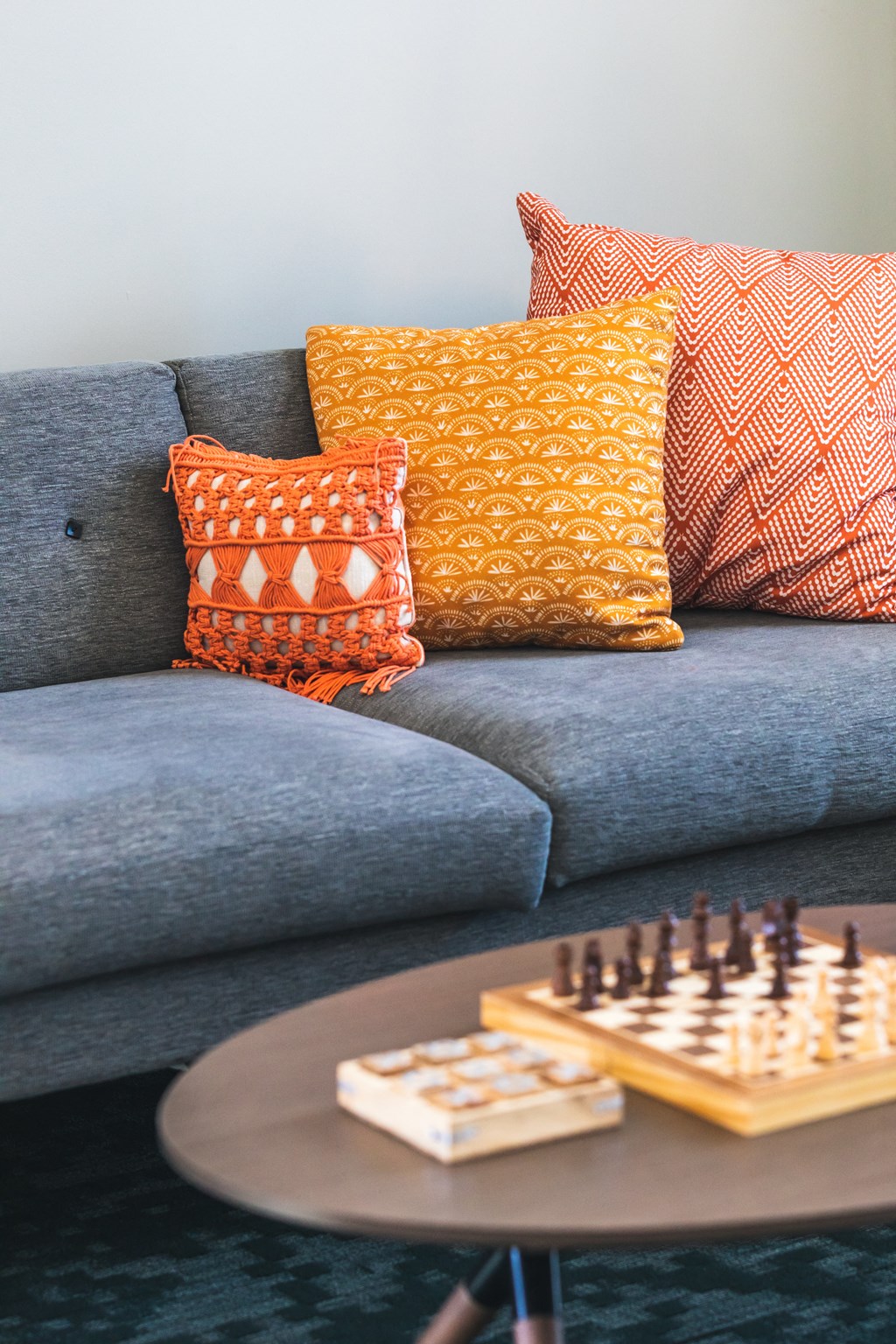 A grey couch with three pillows and a chess board on a table.