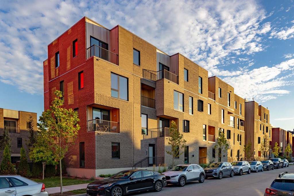 A row of modern apartment buildings with cars parked in front.