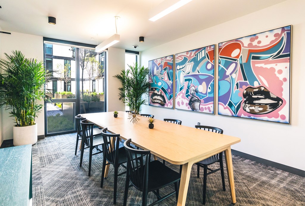 A conference room with a long table and chairs, a potted plant, and a colorful mural on the wall.