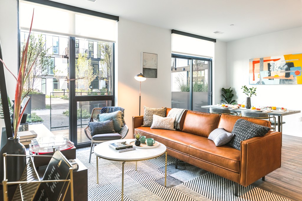 a living room with a brown leather couch and a dining room table in the background