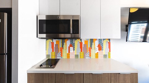 a kitchen with white cabinets and a microwave and a colorful wall mural