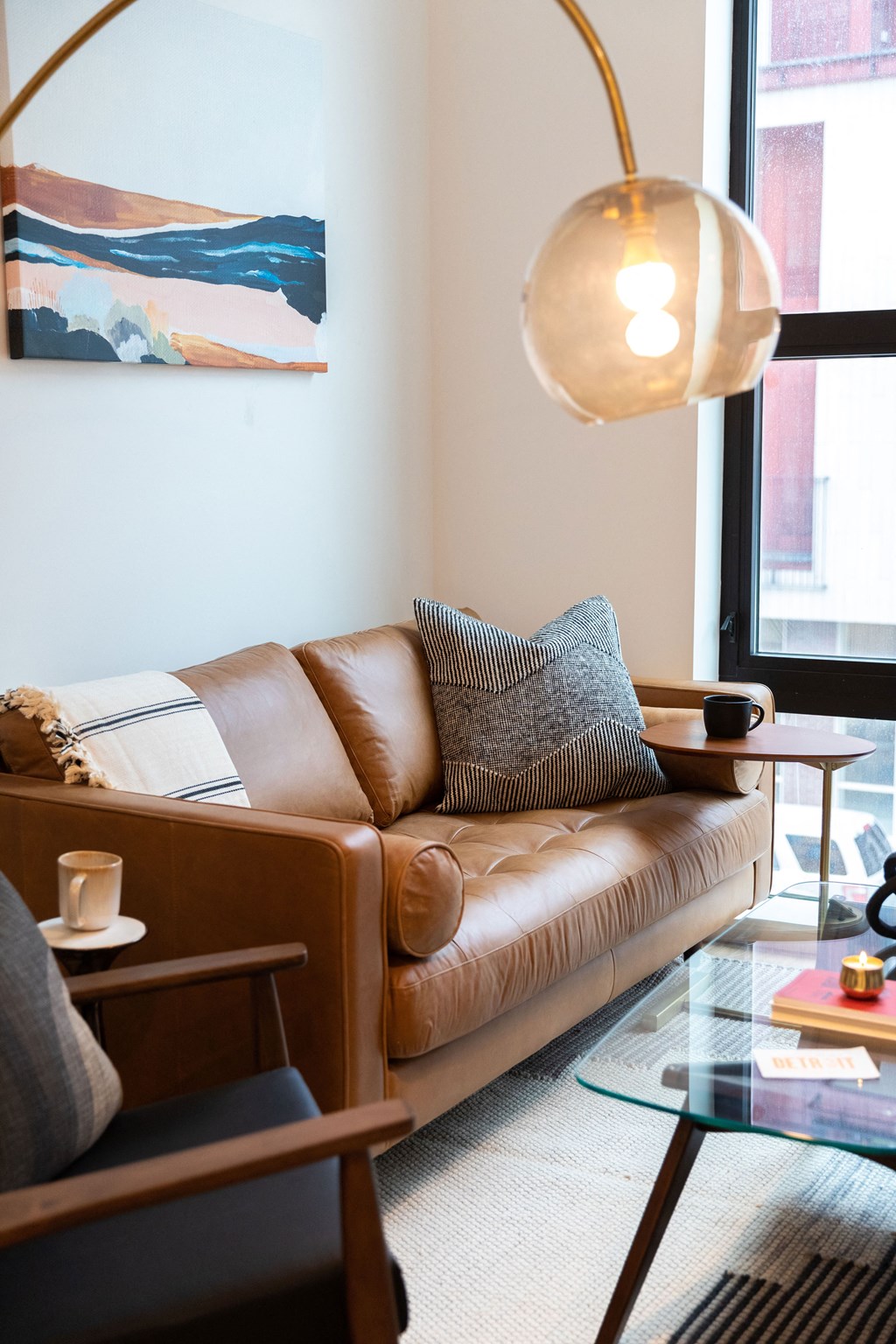 A brown leather couch with a grey pillow and a small table with a cup on it.