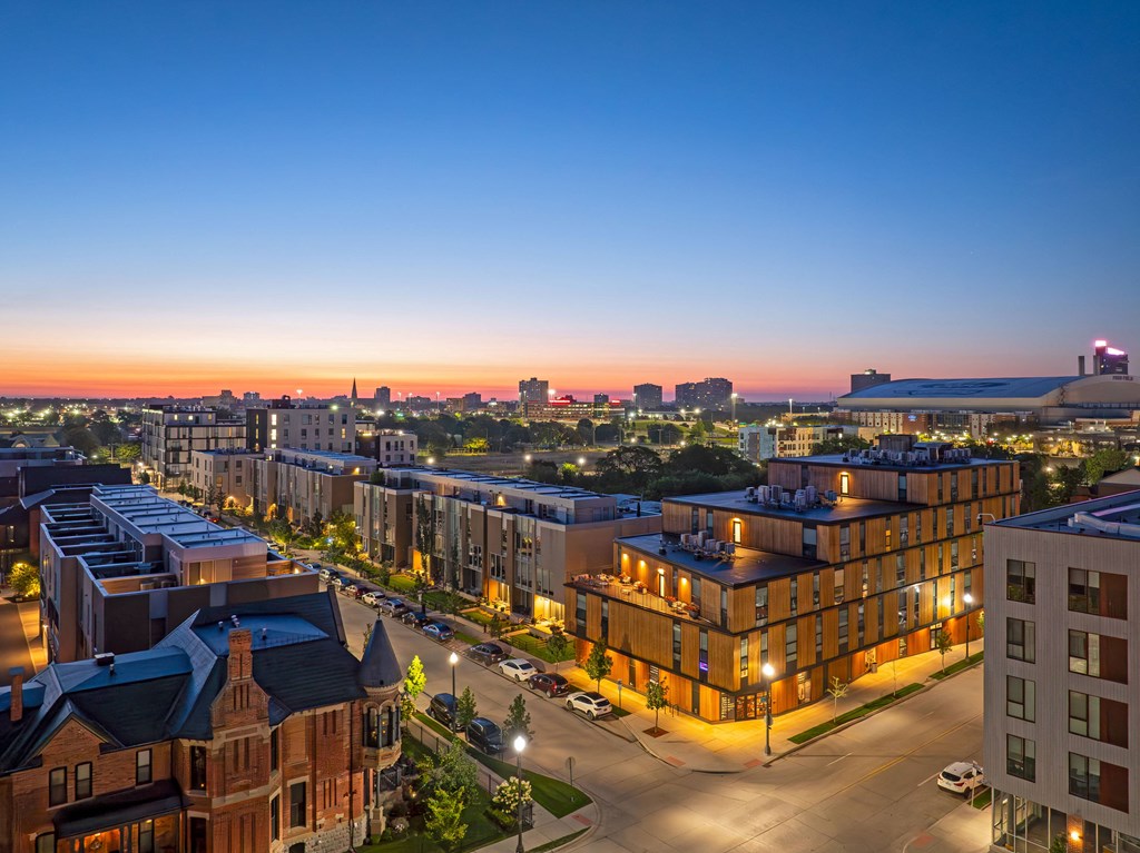 A cityscape at dusk with buildings illuminated and a clear sky.