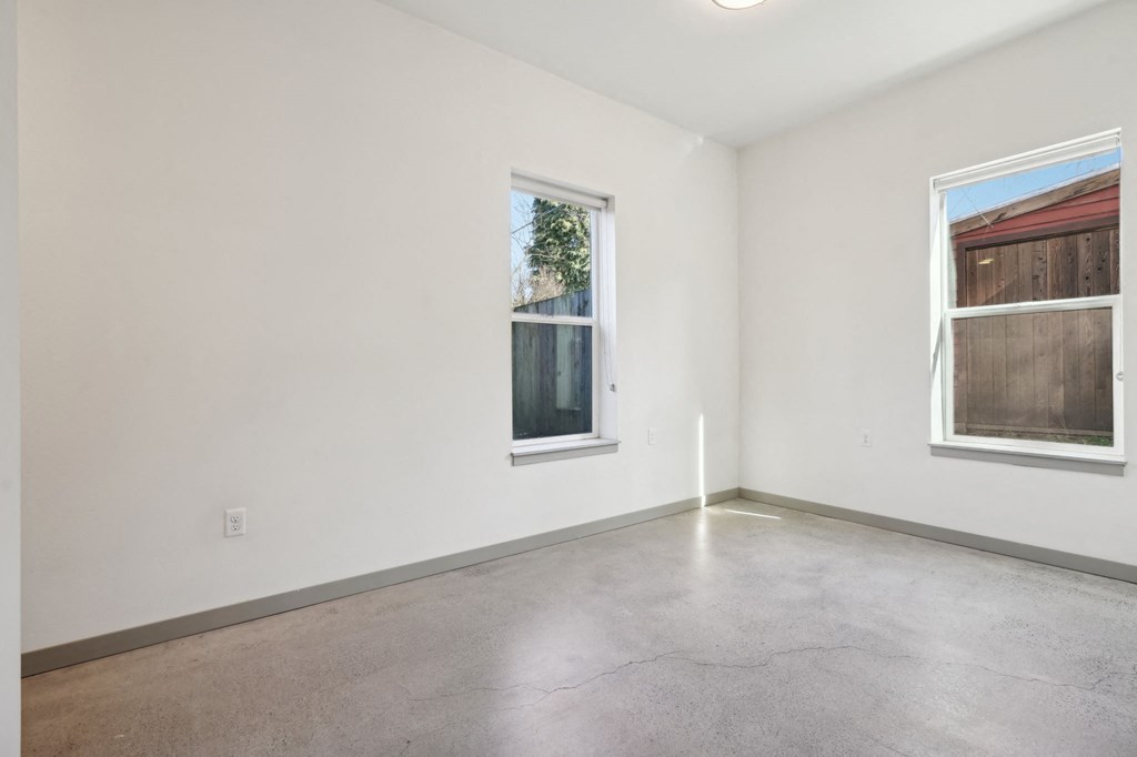 Empty room with a window and a view of a fence and a building outside.